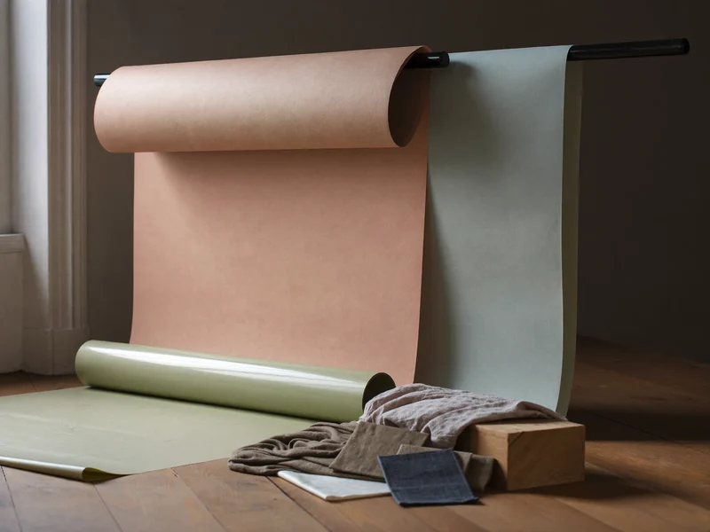 Rollen farbiger Hintergrundpapiere und Materialmuster an der Studiowand im Fensterlicht